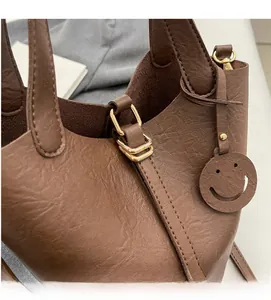 Close-up of brown leather bucket bag featuring gold hardware and a smiley face charm