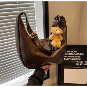 Detail of dark brown dumpling bag with golden buckle and cute plush bear charm