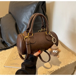 Close-up of a brown leather Boston bag with embossed text and a plush monster charm