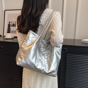 Metallic silver quilted tote bag with pearl pendant and woven chain strap on a model