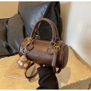 Detailed view of dark brown Boston bag with brand embossing and plush monster charm