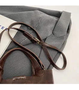 Détail de la bandoulière réglable avec boucle en métal sur un sac seau marron de bureau