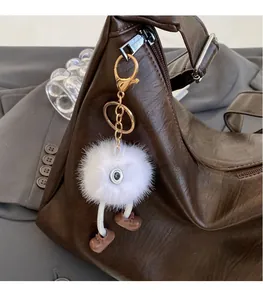 Close-up of white plush cartoon ball charm with brown boots on a leather handbag
