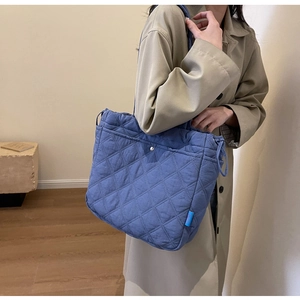 Detail of blue quilted tote bag on shoulder over beige trench coat with blue brand label