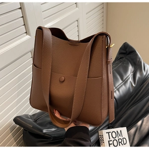 Detalle del bolso tipo cubo en cuero marrón oscuro con textura de grano y correa ancha
