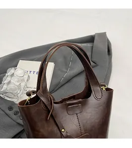 Détail du sac seau en cuir marron foncé avec larges anses et boucle au design rétro