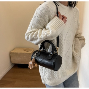Model wearing a black cylindrical Boston bag with gold hardware and plush charm detail