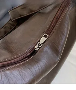 Detailed close-up of a silver polished metal zipper head on a dark brown pebbled leather bag