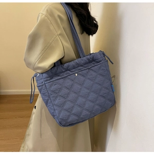 Blue quilted tote bag detail featuring diamond stitching and side drawstring on model