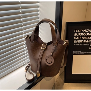 Detail shot of a dark brown pebble leather bucket bag with a gold lock and smiley charm