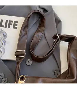 Detail of adjustable smooth leather shoulder strap with silver buckle on dark brown crossbody bag