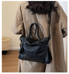 Detail of black pebbled leather tote bag with silver rivets and decorative tassel charms