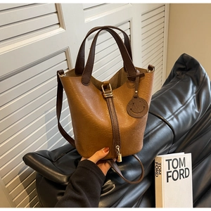 Detail shot of a brown bucket bag with a gold padlock and smiley face charm