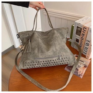 Dettaglio borsa tote in pelle grigio-verde con rivetti e nappe eleganti su una scrivania