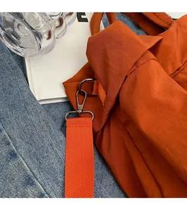 Detail der orangefarbenen Nylon-Beuteltasche mit grauem Metallkarabiner auf Denim