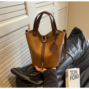 Detail of a brown bucket bag with golden metal lock and round smiley face charm