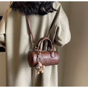 Detail of dark brown Boston bag with brand embossing and a cute plush monster charm