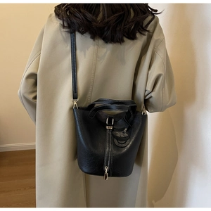 Detail of black leather bucket bag with contrast stitching and metal lock shown on model