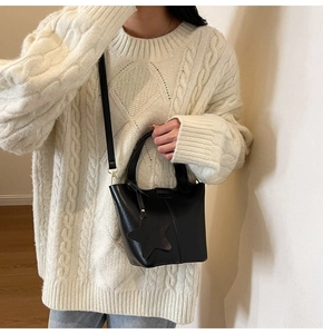 Détail du sac seau noir en similicuir avec breloque étoile sur un pull en maille beige