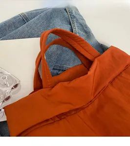 Detailansicht aus Nylonstoff und breitem Griff einer orangefarbenen Stepptasche