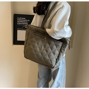 Detail of quilted olive nylon tote bag featuring side drawstrings and metal buckle pocket