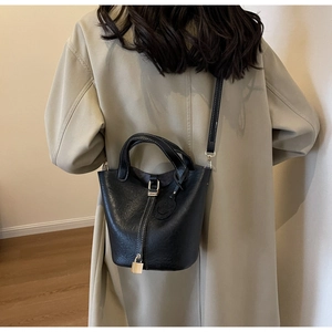 Detail of black lychee leather bucket bag with white stitching and metal lock on a model
