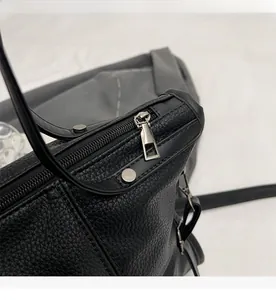 Close-up of smooth metal zipper and rivet details on black lychee grain leather tote