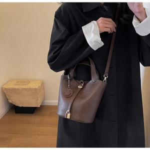 Detail of a brown leather bucket bag with a golden lock and a smiley face charm accessory