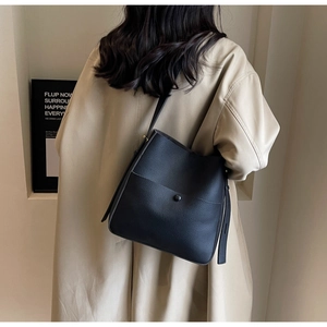 Detalle de bolso cubo negro con textura lichi y bolsillo de presión sobre gabardina beige
