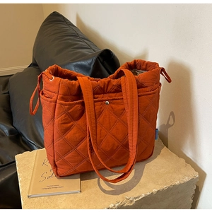 Detail of burnt orange quilted tote bag with side drawstring and high-density fabric texture
