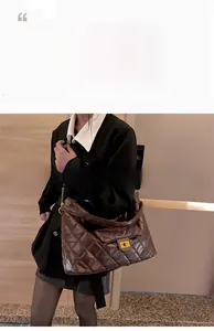 Detail of dark brown quilted leather bag with gold square clasp and chain strap