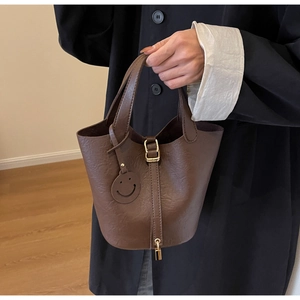 Detailed view of dark brown pebbled leather bucket bag with golden lock and smiley charm