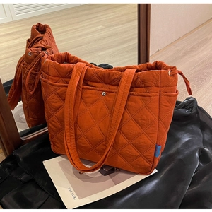 Close-up of orange quilted nylon tote bag with diamond pattern and blue side label detail