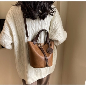 Close-up of brown leather bucket bag with top handles and cute smiley face charm detail