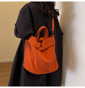 Makroaufnahme einer leuchtend orangen Nylontasche mit abnehmbarem Gurt am Model im Mantel