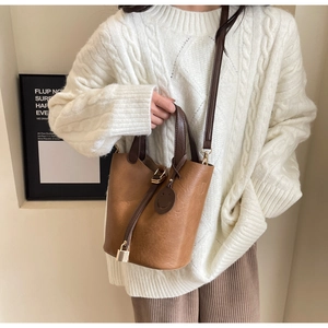Close-up of retro brown leather bucket bag with smiley charm on a knit sweater model