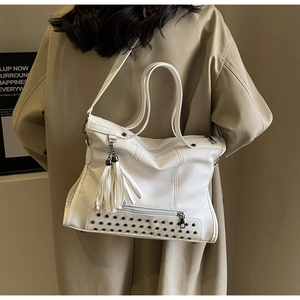 Detail of white pebbled leather tote bag with silver rivets and fringe tassel on model