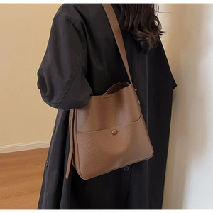 Detalle del bolso tipo cubo de cuero marrón con textura en modelo con abrigo negro