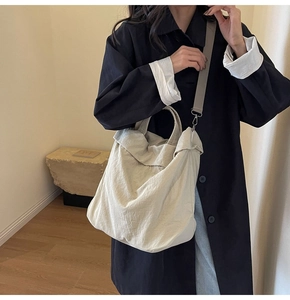 Detail der beigen Nylon-Beuteltasche mit Falten und verstellbarem Gurt auf dem Holzboden