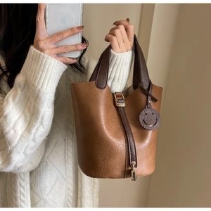 Detail of retro brown bucket bag with contrast handle and smiley charm on knit sweater
