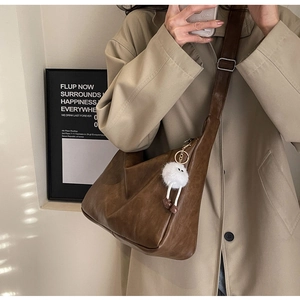 Brown hobo shoulder bag detail with white plush charm on a beige trench coat