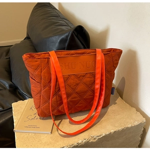 Close-up of quilted caramel orange tote bag with leather handles on stone surface