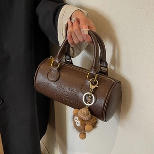 Brown leather Boston barrel bag with top handles and a cute plush bear charm