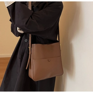 Detalle de bolso bucket de cuero marrón oscuro con bolsillo frontal y correa en un modelo