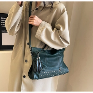Detail view of dark green pebbled leather tote with fringe tassel and metal rivets