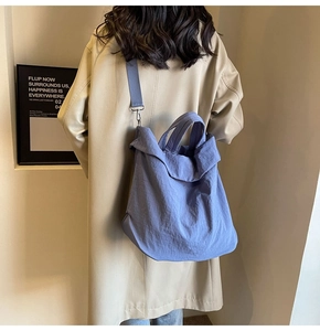 Detailansicht der großen blauen Nylon-Tasche mit breitem Gurt an Modell in Trenchcoat