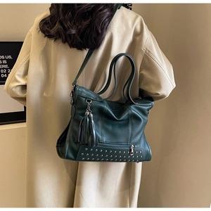 Dark green leather tote bag with silver studs and tassel detail on female model