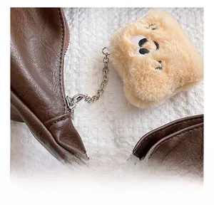Close-up of a cute beige plush bear pendant on a vintage brown leather tote bag detail