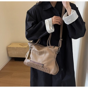 Detail of coffee brown leather tote bag featuring triple row metal rivets and tassel charm
