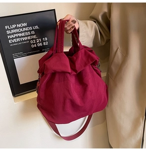Burgunderrote Nylon-Eimertasche mit Faltenstruktur, getragen von einem Modell im Mantel